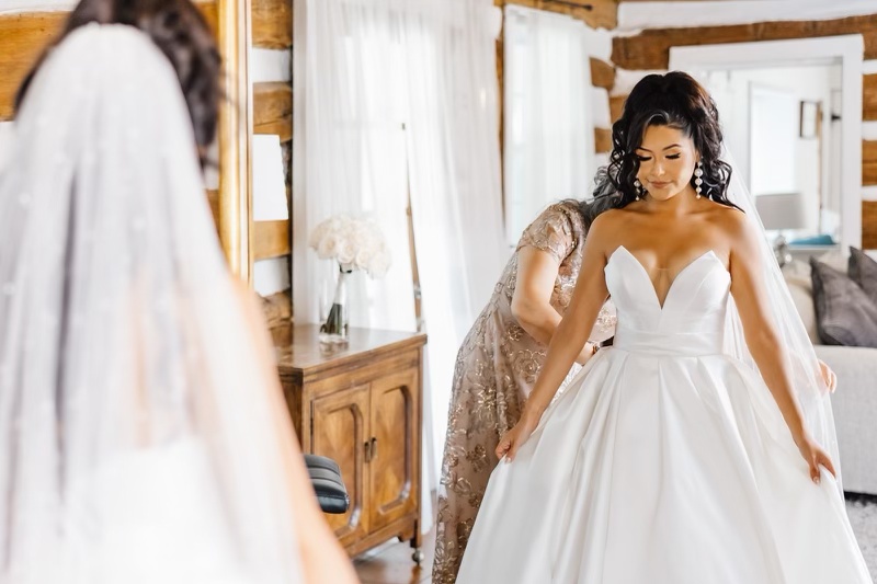 Bride getting ready in a wedding dress with a helping hand in a beautifully decorated room.